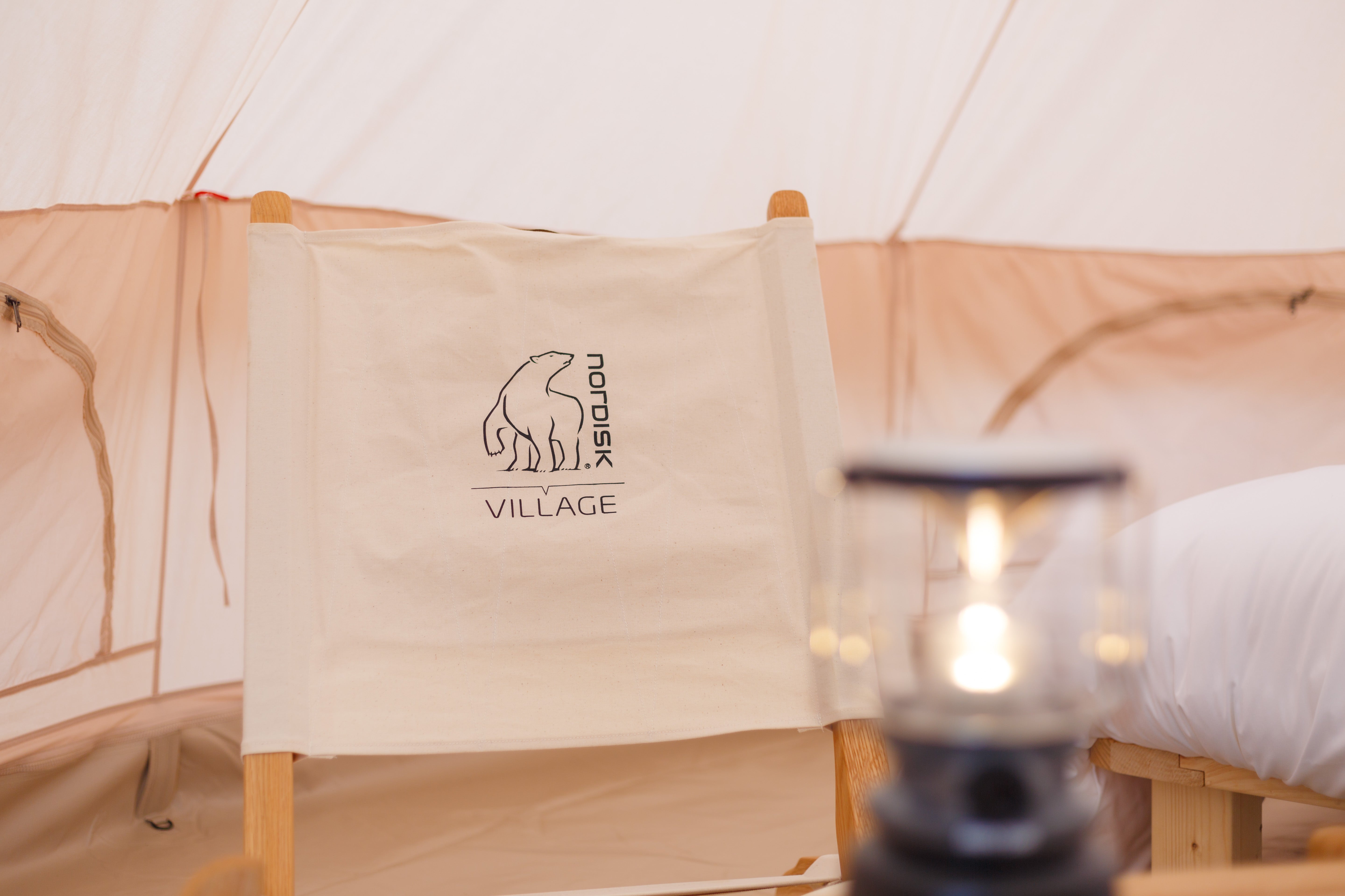 Nordisk Village teltinteriør lounge med Nordisk-logoet på en stol og en lanterne