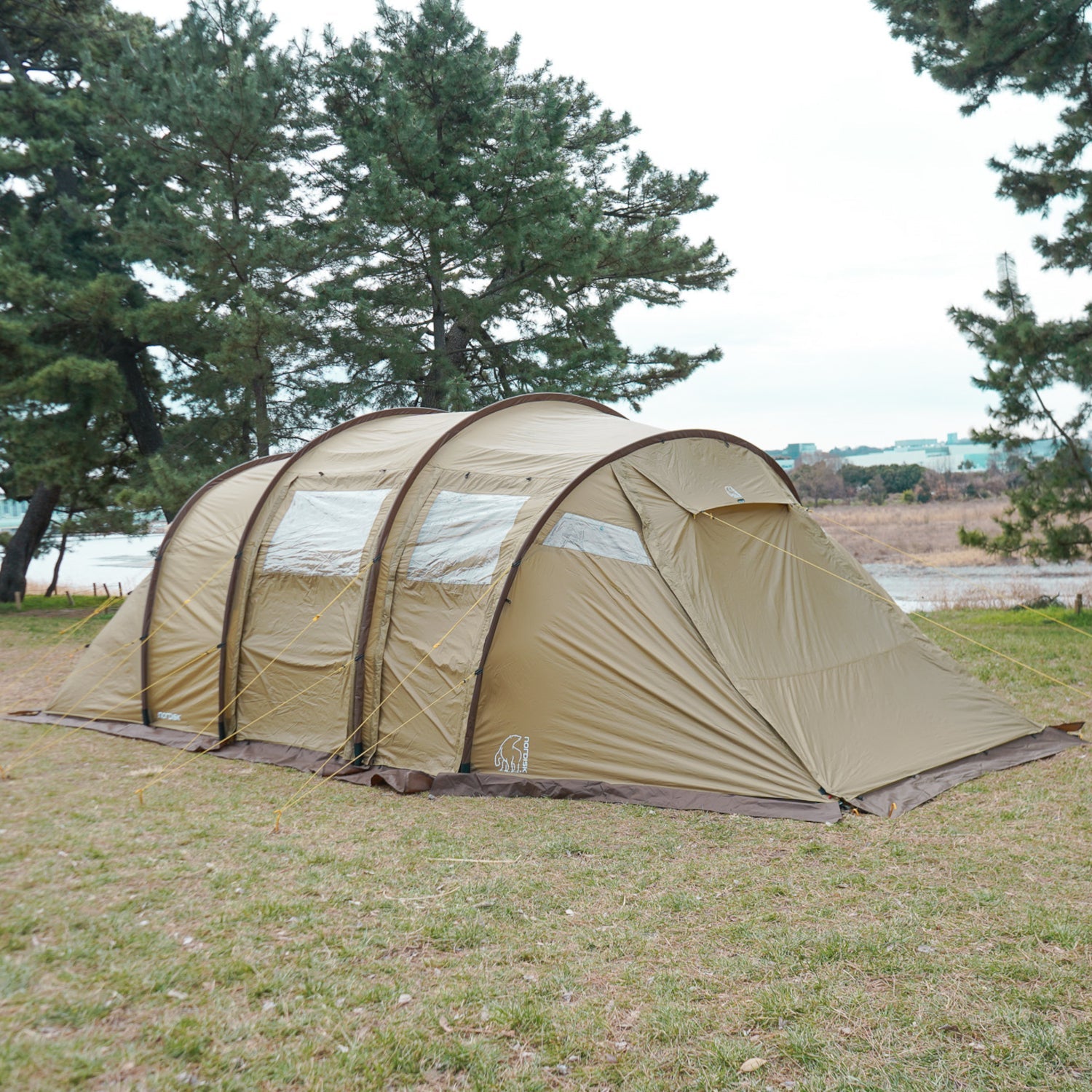 Beige camping tent set up in a grassy area with trees and water in the background