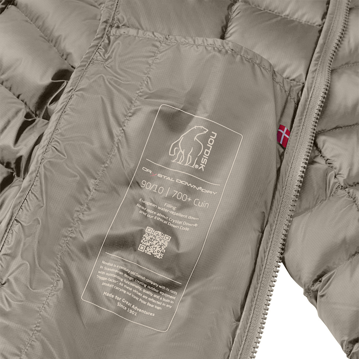 Close-up of a puffer jacket interior showing a large white technical label with the Polaroid logo and text for 900 D / 700+ Cuin, plus a small red Nordic flag tag near the zipper.