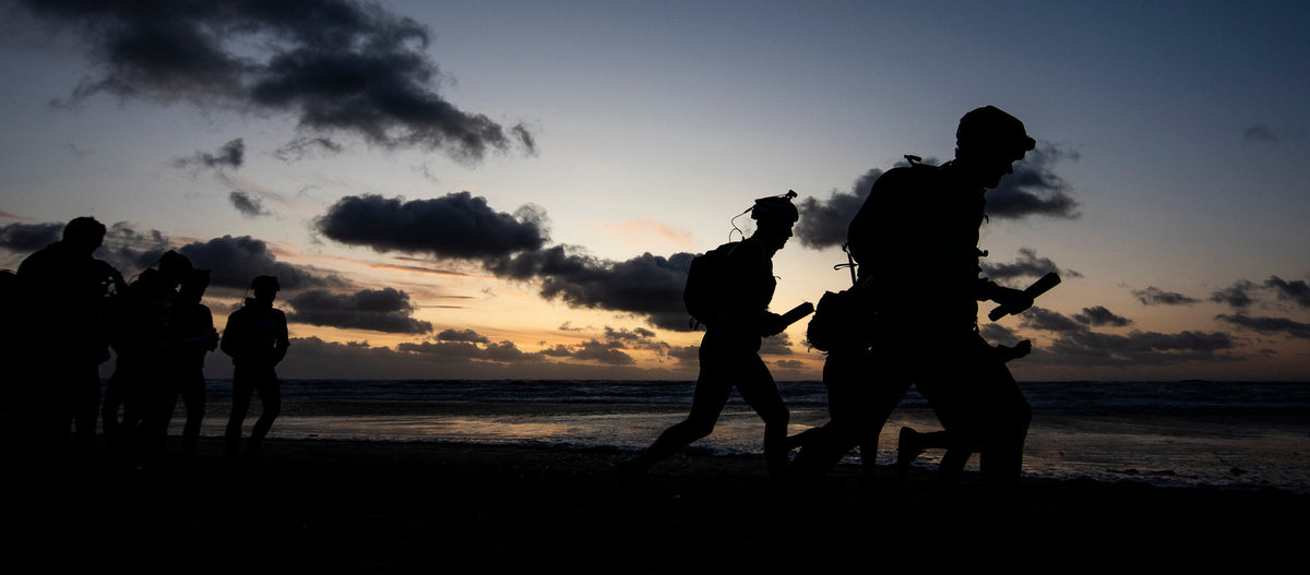 Silhuetter af adventure racere løber på stranden ved solnedgang