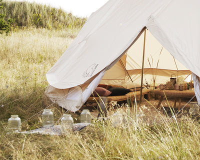 Glampingtelt ved vand med lyskæde og campingudstyr i solnedgang