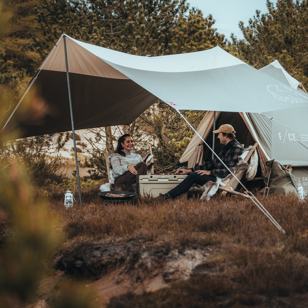Two people sitting under a large tent in a forested area.