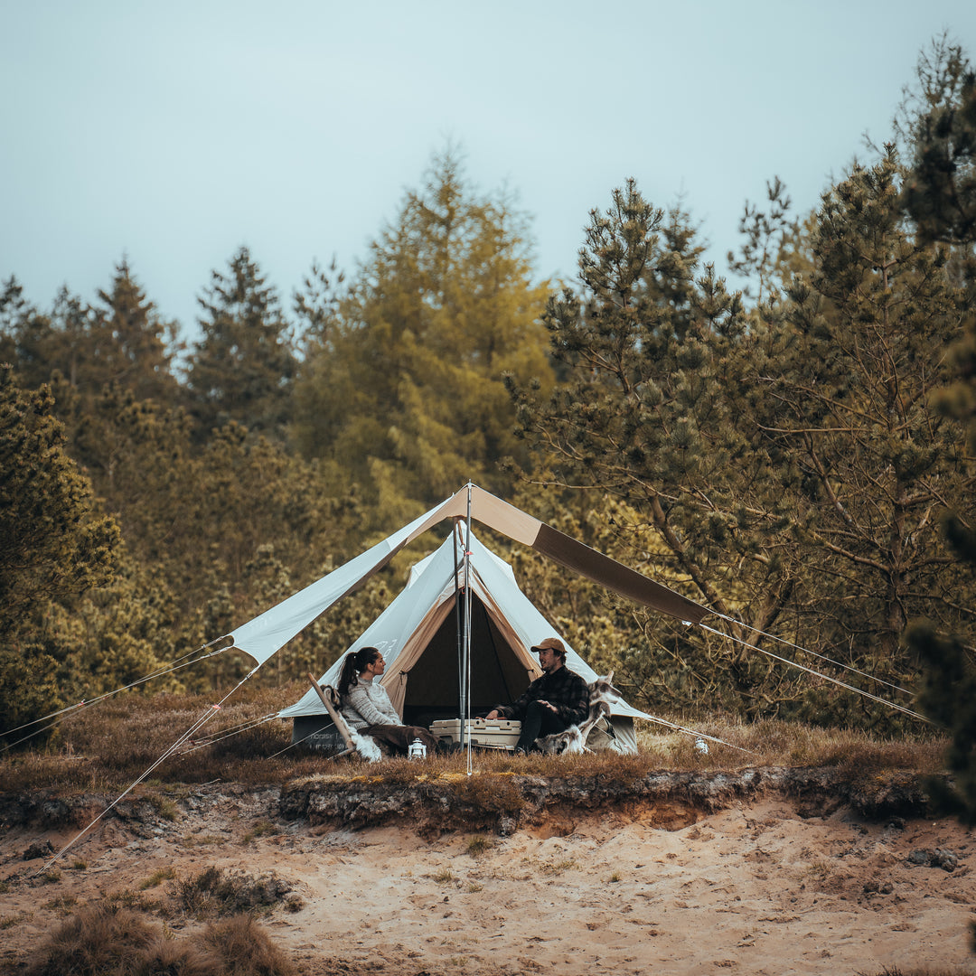 Two people sitting in front of a tent in a forest setting