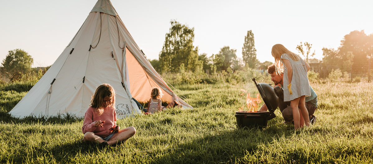 Familie hygger sig med grill og telt udendørs i naturen ved solnedgang