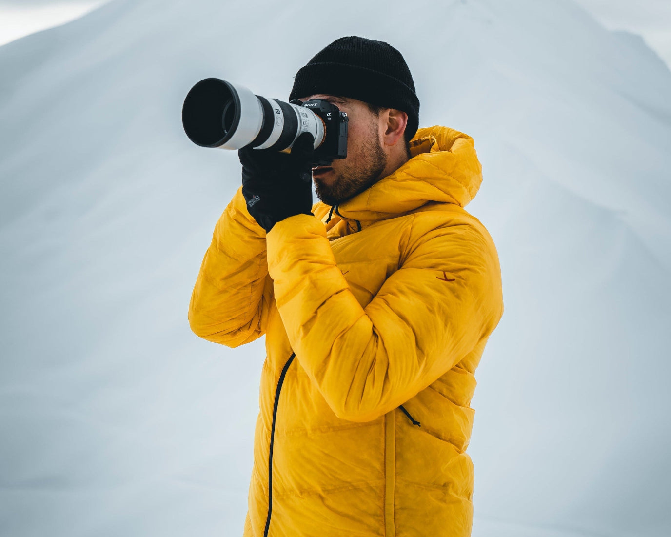 Mand i gul jakke fotograferer med kamera i snedækket landskab