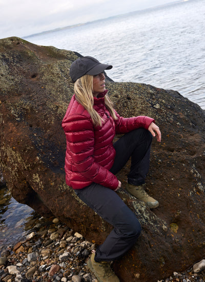 Kvinde i Companyon Thyra dunjakke i Tibetan Red på en klippe ved havet