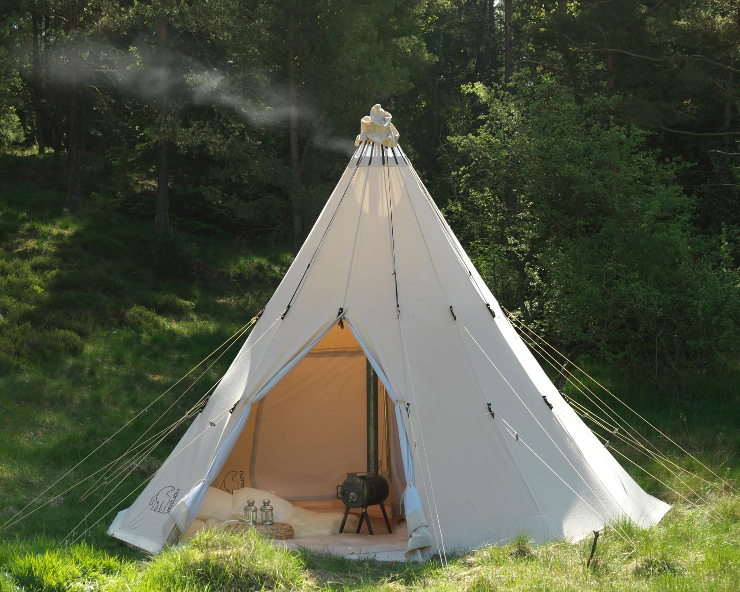 Glamping telt, bål i forgrunden, mand griller i skoven